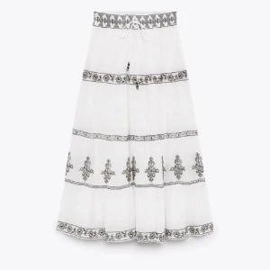 Vit långkjol Zara - Vit långkjol med svarta broderade mönster och knytband i midjan. Kjolen har flera dekorativa bårder och ett lätt, luftigt tyg som ger en bohemisk känsla. Perfekt för varma dagar och stilrena outfits. Kjolen säljs inte längre💕