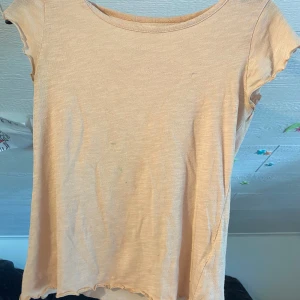 Ljusrosa t-shirt från 157 Angelology - Säljer en ljusrosa t-shirt från Angelology i storlek XS. Toppen har korta ärmar, rund halsringning och ett broderat motiv av rosa vingar i nacken. Perfekt för en enkel och stilren look.