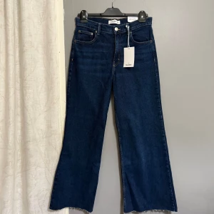 Mörkblå wide leg jeans från Pull&Bear - Säljer ett par mörkblå jeans från Pull&Bear med wide leg-modell och råa benslut. Byxorna har klassisk femficksdesign, knapp och dragkedja i gylfen samt midwaist passform. Perfekta för en trendig och avslappnad look.