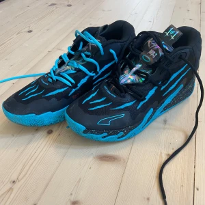 Puma MB.03 Blue Hive sneakers - Säljer ett par Puma MB.03 Blue Hive sneakers i svart och blått med unika detaljer och mönstrad sula. Skorna har snörning och coola grafiska inslag, perfekta för dig som vill sticka ut med din stil. Använda utomhus ca 2-3 gånger.