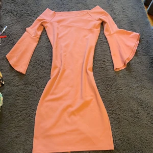 Rosa klänning med trumpetärmar - Rosa klänning med snygga volangärmar och figurnära passform. Klänningen har en offshoulder-skärning och är tillverkad i ett mjukt, stretchigt material. Från River Island, storlek 8 vilket motsvarar typ 36. Oanvänd men kommer utan prislapp.