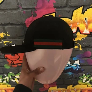 Svart keps från Gucci med grön-röd rand - ÄKTA Gucci keps nya modellen! Säljer en svart keps från Gucci med klassisk grön och röd rand på sidan. Kepsen har böjd skärm och justerbar passform. Tillverkad i Italien och har märkets logotyp invändigt. 