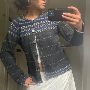 Mörkgrå mönstrad kofta med blå detaljer - Säljer en mysig mörkgrå kofta med blått och vitt mönster från indiska. Koftan har rund halsringning, långa ärmar och knäpps med svarta knappar framtill. Perfekt för lager-på-lager och passar till många olika stilar. Mycket bra skick!🥰