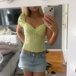 Ljusgul korsett-topp med dragkedja - Trendig ljusgul korsett-topp med korta puffärmar och markerad byst. Toppen har en snygg dragkedja framtill och figurnära passform. Perfekt för dig som vill sticka ut med en färgglad och feminin look.