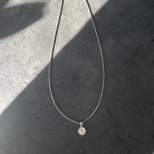 Silverhalsband med rund glittrig berlock - Ett stilrent halsband i silverfärg med en tunn kedja och en rund, glittrig berlock som reflekterar ljuset fint. Perfekt för dig som gillar enkla men eleganta smycken.