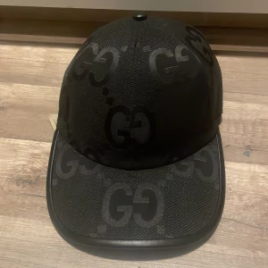 Svart keps från Gucci - Snygg svart keps från Gucci med det ikoniska GG-mönstret. Kepsen har en justerbar rem baktill för perfekt passform. Tillverkad i ett slitstarkt material med en stilren design.