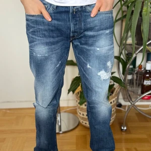 Blå jeans från Replay - Blå jeans från Replay med slitna detaljer. Dessa jeans har en normal passform och är perfekta för en avslappnad stil. Märket Replay syns tydligt på fickan och insidan av midjan. Hör av dig för minsta fundering så löser vi de tillsammans, pris diskuterbart🙌😌