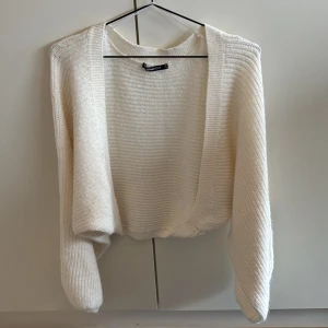 Vit stickad bolerotopp från Gina Tricot - Säljer en stilren vit stickad bolerotopp från Gina Tricot. Perfekt för lager-på-lager och har en öppen design som ger en avslappnad look. Passar bra till både vardag och festliga tillfällen.