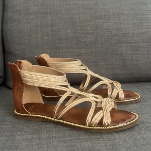 Beige sandaler med flätad design - Eleganta, och väldigt fina sandaler i storlek 40. Perfekta att använda på sommaren. De är från Bata i beige färg med flätad design och öppen tå. De har en brun sula och en elegant snörning runt ankeln. Färgerna, formen, alltså dessa sandaler är väldigt vackra som passar både tjejer och damer. Såna här sandaler kostar omkring 1000-1500 kronor från Bata, men eftersom de inte kommer till användning av min mamma så säljer jag dem väldigt billigt 