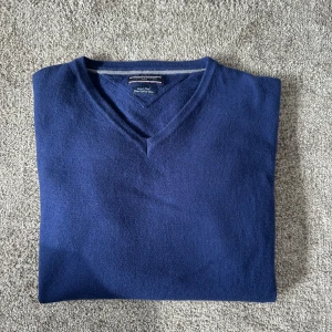 Blå v-ringad tröja från Tommy Hilfiger  - Säljer en stilren blå v-ringad tröja från Tommy Hilfiger. Tröjan är i nyskick och sparsamt använd. Tröjan är i 100 % merinoull. Storlek xs, pris 249. Skriv vid frågor. 