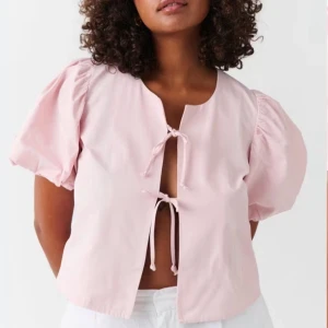 Rosa blus med puffärmar och knytband - Söt rosa blus med korta puffärmar och knytband framtill. Perfekt nu för våren och sommaren.Endast använd fåtal gånger!