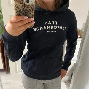 Svart hoodie från Peak Performance - Säljer en svart hoodie från Peak Performance med vit text på bröstet. Tröjan har en klassisk design med huva och en stor ficka framtill. Perfekt för en avslappnad stil. PRISET GÅR ATT PRUTA!