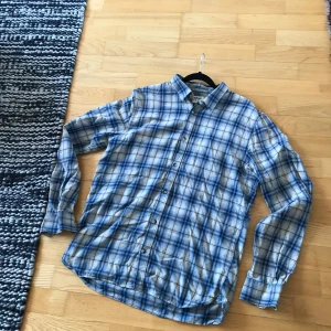 Flanell skjorta från Dobber - Säljer en snygg blå och vit rutig skjorta från Dobber. Skjortan har långa ärmar och knappar framtill. Perfekt för en avslappnad stil. Mycket bra skick förutom en rand på ryggen som syns i bilderna. (randen går inte bort).