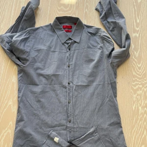 Grå skjorta från Hugo Boss Slim fit - Snygg grå skjorta från Hugo Boss i slim fit. Skjortan har långa ärmar och knappar framtill. Perfekt för en stilren look.