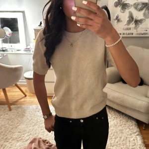 Beige stickad tröja - Säljer en stilren beige stickad tröja med korta ärmar. Perfekt för en avslappnad look. Tröjan har en rund halsringning och är gjord i ett mjukt material.