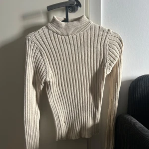 Beige ribbad polotröja från Rut&Circle - Säljer en stilren beige ribbad polotröja från Rut&Circle. Tröjan har en hög krage och långa ärmar, perfekt för kyligare dagar. Den är både bekväm och trendig, ett måste i garderoben!