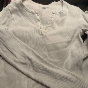 Vit ribbad långärmad topp från Brandy Melville - Säljer en vit ribbad långärmad topp från Brandy Melville. Toppen har en knappdetalj framtill och en bekväm passform. Perfekt för en avslappnad stil. Hör av dig vid intresse!