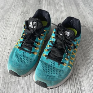 Nike Zoom Pegasus 32 löparskor - Snygga turkosa Nike Zoom Pegasus 32 löparskor med svarta och gula detaljer. Skorna har svart snörning och en ventilerande ovandel. Perfekta för löpning och träning. Storlek EU 38