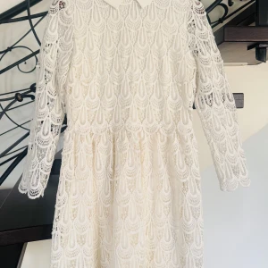 Vit spetsklänning från Sand - Elegant vit spetsklänning från Sand med långärmad design och en klassisk krage. Klänningen har ett vackert spetsmönster och en dragkedja i ryggen för enkel påklädning. Perfekt för speciella tillfällen. Mycket fin skick, inga skavanker eller fläckar .Nypris: 3800.-