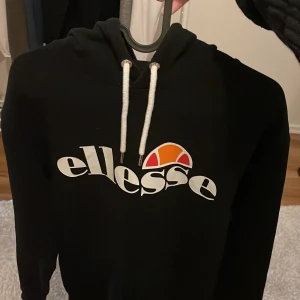 Svart hoodie från Ellesse - Säljer en svart hoodie från Ellesse med vit logga och snören. Perfekt för en avslappnad stil. Den har en klassisk design med huva. Originalpris 500