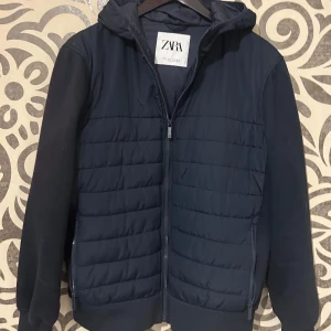 Mörkblå jacka från Zara - Snygg mörkblå jacka från Zara med dragkedja och huva. Jackan har långa ärmar och quiltad design framtill. Perfekt för vårdagar. 