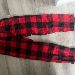 Röd och svart rutig byxa från H&M pyjamasbyxor  - Snygga röd- och svartrutiga byxor från H&M med en bekväm passform. Byxorna har en elastisk midja med snörning för extra komfort. Perfekta för en avslappnad stil.