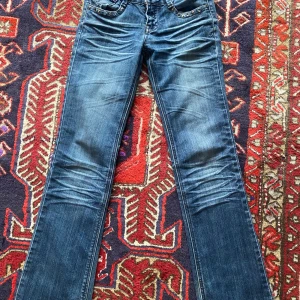 Blå jeans med nitar - Snygga blå jeans med bootcut-stil och coola nitar på fickorna. De har en låg midja och är dekorerade med rynkade detaljer på benen💕