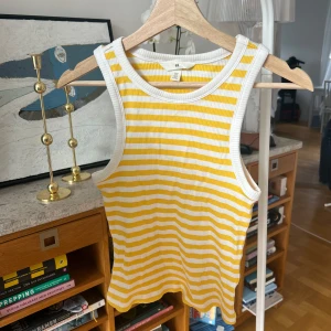 Gul- och vitrandig linnetopp från H&M - Säljer en fräsch gul- och vitrandig linnetopp från H&M. Toppen är ribbad och ärmlös, perfekt för varma sommardagar. Den har en bekväm passform och är gjord i mjukt material. Perfekt för en avslappnad stil! 🌞
