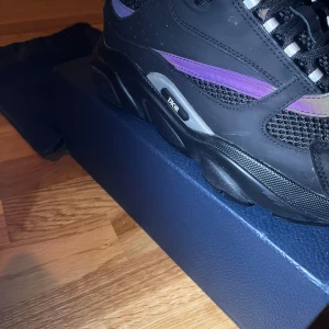 Svarta sneakers från Dior - Snygga svarta sneakers från Dior med färgglada detaljer i lila och turkos. Skorna har en robust sula och snörning framtill. Perfekta för en trendig look.