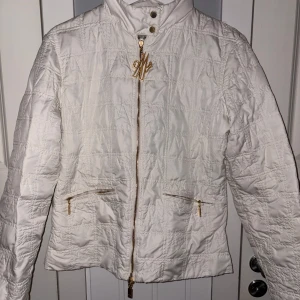 Vit moncler jacka - Säljer en stilren vit quiltad jacka från Moncler med guldfärgade dragkedjor och knappar. Jackan har en hög krage och ett elegant mönster. Perfekt för kyligare dagar och ger en lyxig känsla. 🧥✨