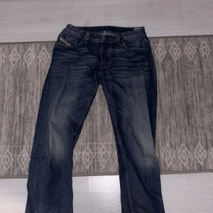 Blå jeans från Diesel - Säljer ett par klassiska blå jeans från Diesel, modell Larkee. De har en straight passform med fem fickor och snygga detaljer vid bakfickorna. Perfekta för en avslappnad stil. Insydda i sidorna men går enkelt att sprätta om behovet finns!