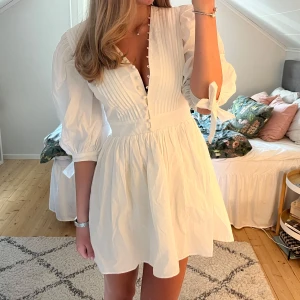 Vit klänning från Showpo - Säljer en söt vit klänning från Showpo med puffärmar och knappar framtill. Klänningen har en v-ringad design och knytband vid ärmsluten. Perfekt för studenten. Har aldrig använt den och prislapp finns kvar🩷