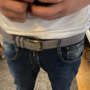 Grått bälte med silverfärgat spänne - Snyggt grått bälte med ett stilrent silverfärgat spänne. Perfekt för att ge en extra touch till din outfit. Bältet är tillverkat i ett material som liknar mocka och har en klassisk design.