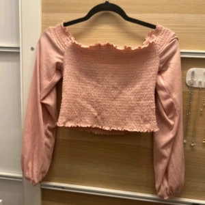 Rosa topp - Säljer en söt rosa smockad topp med långa ärmar och en volangdetalj vid hals och nederkant. Perfekt för en trendig look! 💖