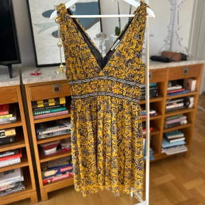 Gul blommig klänning från Isabel Marant Étoile - Säljer en vacker gul klänning från Isabel Marant Étoile med blommigt mönster i svart. Klänningen har en v-ringad design. Perfekt för en somrig look! Storlek 36.