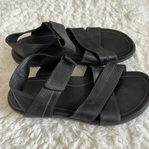 Svarta sandaler från Ecco  - Säljer ett par svarta Ecco herrsandaler i läder. Snygga och bekväma svarta sandaler från Ecco med justerbara remmar för perfekt passform. STORLEK 42. Helt nya, oanvända. Pris kan diskuteras 
