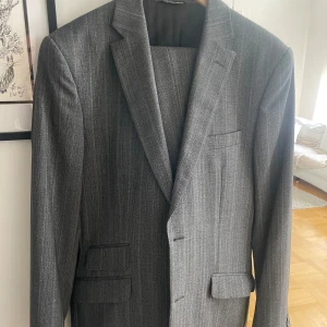 Dolce & Gabbana kostym grå  - Snygg grå kostym med diskreta ränder. Kavajen har klassisk passform med två knappar och fickor med lock. Material Lana Woll. Byxorna är raka och matchar kavajen perfekt. Har använts två gånger. Ny pris ca 17000kr  Storlek 50  