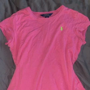 Rosa t-shirt från Ralph Lauren - Säljer en snygg rosa t-shirt från Ralph Lauren med korta ärmar och en liten grön logga på bröstet. Perfekt för en avslappnad stil. 💖 Den är i storlek L i barnstorlek men passar xs och s