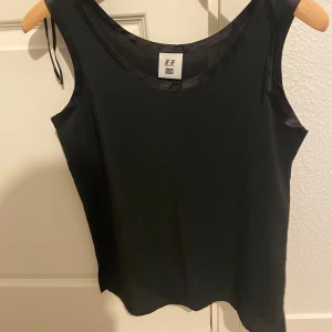 Svart linnetopp från Euro Fashion - Snygg svart linnetopp från Euro Fashion i ett glansigt material. Perfekt för en stilren look. Toppen har en enkel design med rund halsringning.