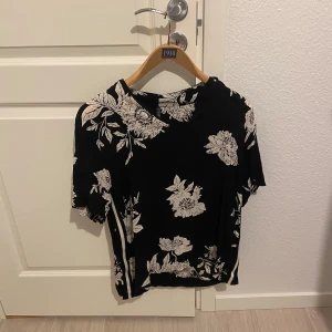 Svart blommig topp från Freequent - Säljer en svart topp från Freequent med ett vackert blommönster i vitt. Toppen har korta ärmar och en bekväm passform. Perfekt för en stilren look.