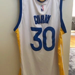 Vit Golden State Warriors basketlinne - Säljer ett vitt Golden State Warriors basketlinne från Nike med blå och gula detaljer. Linnet har spelarnamnet och numret 'Curry 30' på baksidan. Perfekt för basketfans och sportentusiaster! Den är prefekt till sommaren också och vi kan diskutera ett bra pris.