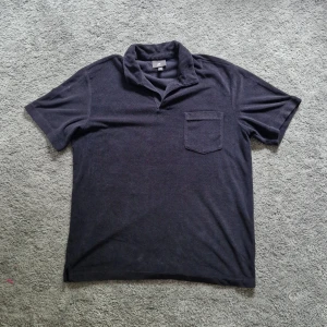 Mörkblå frotté t-shirt med krage - Säljer en mörkblå kortärmad frottéskjorta från H&M med krage och bröstficka. Regular fit och kortärmad modell, perfekt för en avslappnad stil. Passar dig som gillar enkel och stilren design.