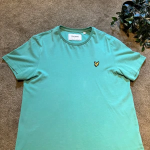 Grön t-shirt från Lyle & Scott - Snygg grön t-shirt från Lyle & Scott med klassisk rund hals och broderad gul logga på bröstet. Tillverkad i 100% ekologisk bomull för en skön och hållbar känsla. Perfekt för en avslappnad stil.