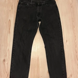 Svarta jeans från Jack & Jones - Säljer ett par svarta jeans från Jack & Jones i klassisk modell. Jeansen har knappgylf och raka ben. Perfekta till vardags och passar till det mesta. Midjemått 32 och längd 30.