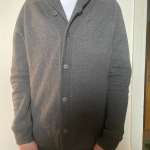 Grå cardigan jacka från J.Lindeberg - Säljer en stilren grå cardigan  från J.Lindeberg. Det är bomulls material, storlek L men passar även för M. Passar för alla väder. Hör av er vid minsta lilla fundering
