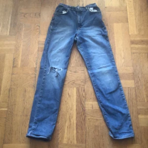 Blå raka jeansbyxor - Klassiska blå jeansbyxor med raka ben och hög midja. Jeansen har en sliten detalj vid ena knät och femficksdesign. Perfekta för en avslappnad stil och passar till det mesta. 200kr + frakt 