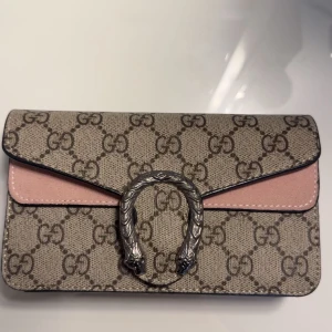 Beige axelväska med rosa detalj. - Säljer en snygg axelväska från  med klassiskt GG-mönster i beige och brunt. Väskan har detaljer i ljusrosa en mörk silverfärgat kedja samt spänne framtill. Otroligt bra skick och extremt bra kvalité!💕 Detta ör sen lilla modellen!