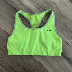 Sport-bh från Nike storlek S - Säljer en neongul sport-bh från Nike med grå kantband och klassisk racerback. Tight passform. Nike-logga framtill. Välanvänd. Svårt att fånga färgen på bild, den är något gulare än vad kameran kan fånga upp på de första bilderna.