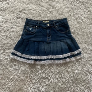 Mörkblå jeanskjol med spetskant - Lågmidjad jeanskjol omsydd från ett par jeans.  Midjemått tvärsöver- 34cm Längd-34cm