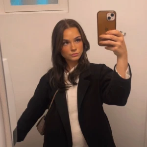 Svart kappa med bälte - Säljer en svart lång kappa med bälte i midjan. Klassisk rak modell med lång ärm och krage. Perfekt för dig som vill ha en stilren och tidlös jacka. Passar till många olika outfits och har en snygg siluett.